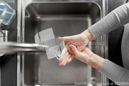 Image of woman washing hands with liquid soap in kitchen