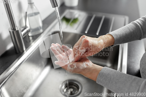 Image of woman washing hands with liquid soap in kitchen