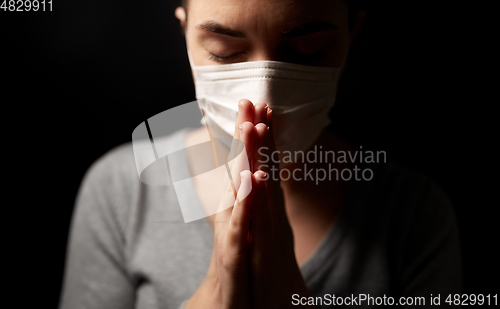 Image of sick young woman in protective face mask praying