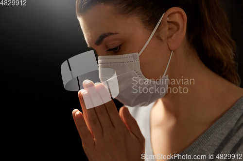 Image of sick young woman in protective face mask praying