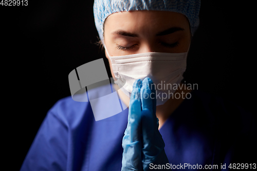 Image of female doctor or nurse in face mask praying