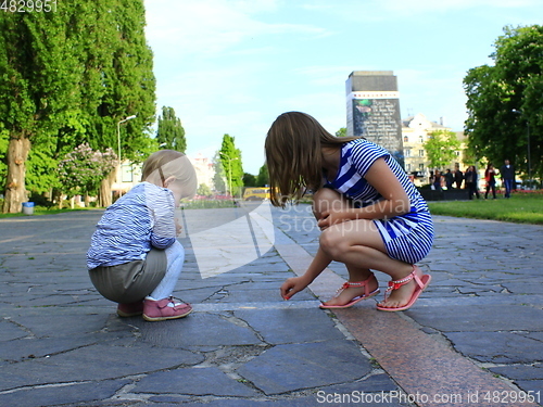 Image of little sisters write on the road in the park