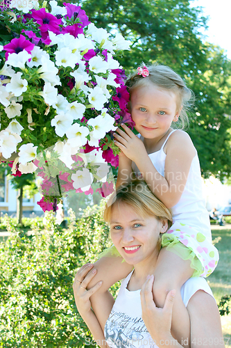 Image of daughter sitting on her mother and many flowers in the city park