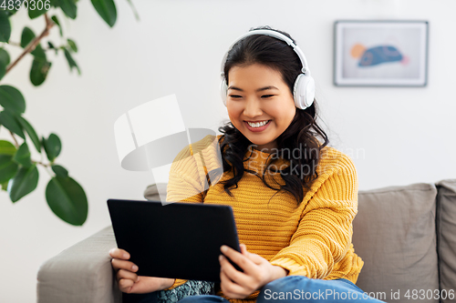 Image of asian woman with headphones and tablet pc at home