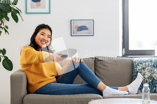 Image of asian woman with tv remote sitting on sofa at home