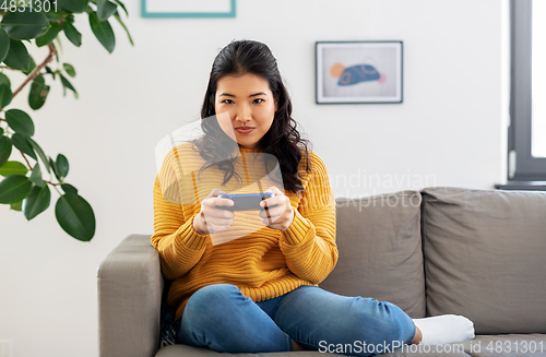 Image of asian woman with gamepad playing game at home