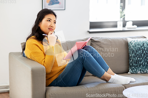 Image of asian woman with diary sitting on sofa at home