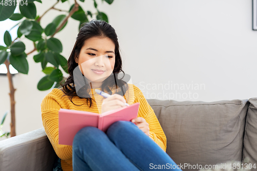 Image of asian woman with diary sitting on sofa at home