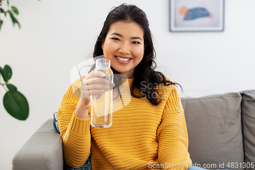 Image of smiling asian young woman drinking water at home