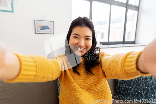 Image of smiling asian young woman taking selfie at home