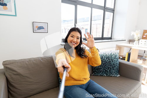 Image of asian woman taking selfie and waving hand at home