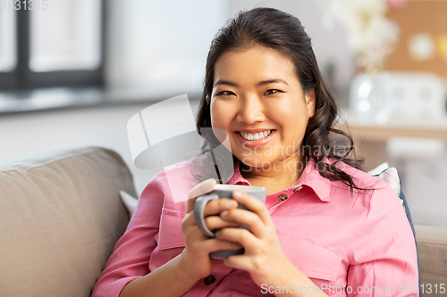 Image of smiling asian young woman drinking coffee at home