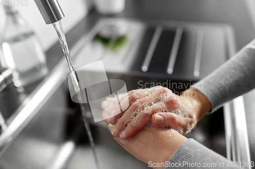 Image of woman washing hands with liquid soap in kitchen