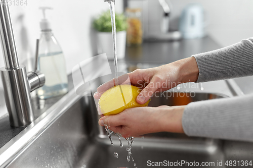 Image of close up of woman washing lemon fruit in kitchen