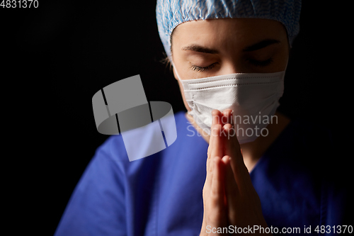 Image of female doctor or nurse in face mask praying