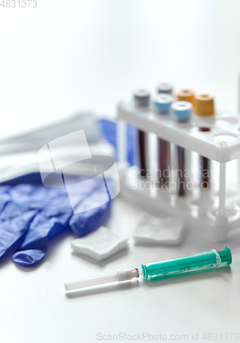 Image of syringe, beakers with blood test, gloves and mask