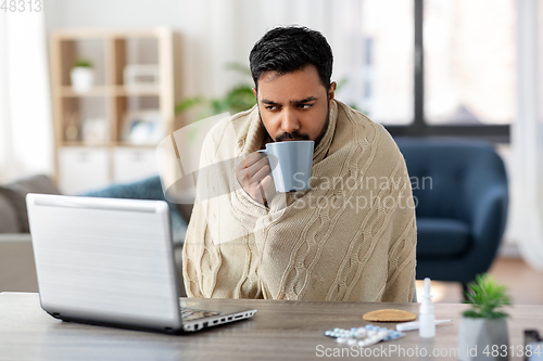 Image of ill indian man in blanket drinking hot tea at home