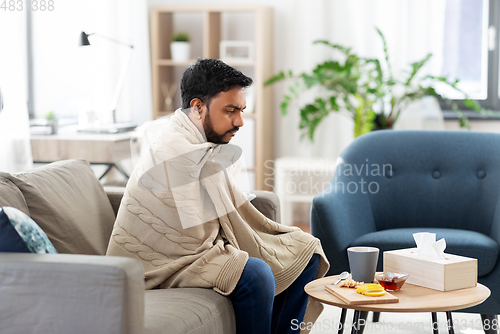 Image of sick young man in blanket with hot tea at home