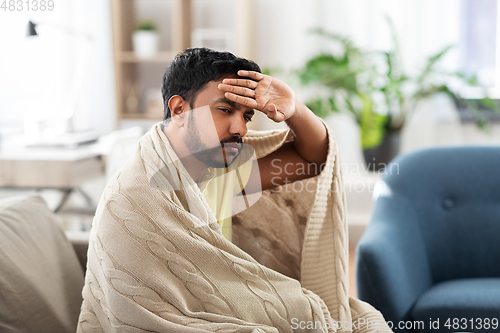 Image of sick young man in blanket having headache or fever