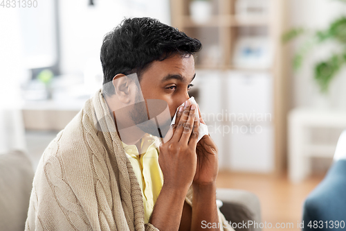 Image of sick man blowing nose in paper tissue at home