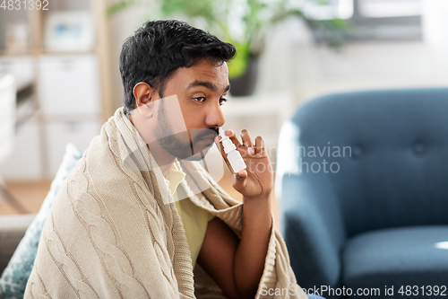 Image of sick indian man using nasal spray at home