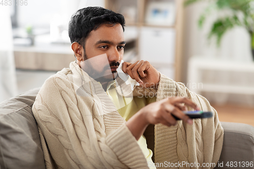 Image of sick man with paper tissue and tv remote at home