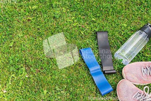 Image of Ladie's fitness rubber bands and sneakers on the green grass background