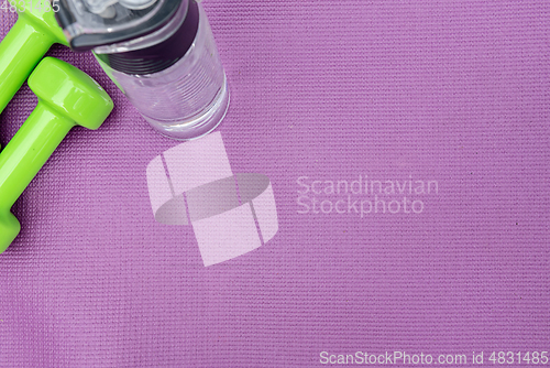 Image of Ladie's dumbbells and water bottle over purple fitness mat, top view.