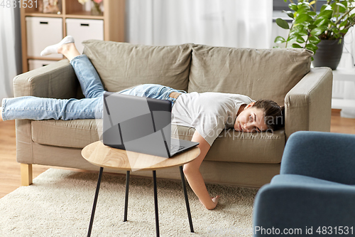 Image of bored woman with laptop lying on sofa at home