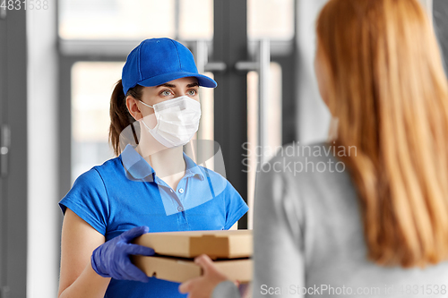 Image of delivery girl in mask giving pizza boxes to woman