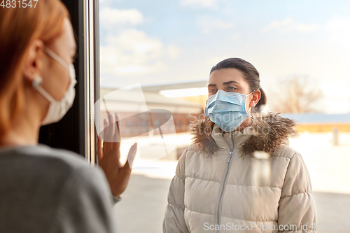 Image of woman in mask looking to friend through window