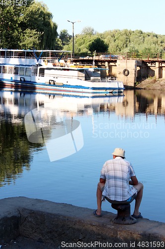 Image of fisherman fishing in the city river near motor ship 