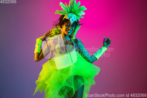 Image of Beautiful young woman in carnival and masquerade costume on gradient studio background in neon light