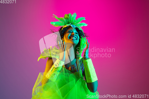 Image of Beautiful young woman in carnival and masquerade costume on gradient studio background in neon light