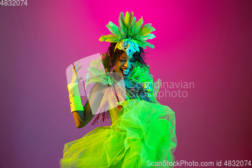 Image of Beautiful young woman in carnival and masquerade costume on gradient studio background in neon light