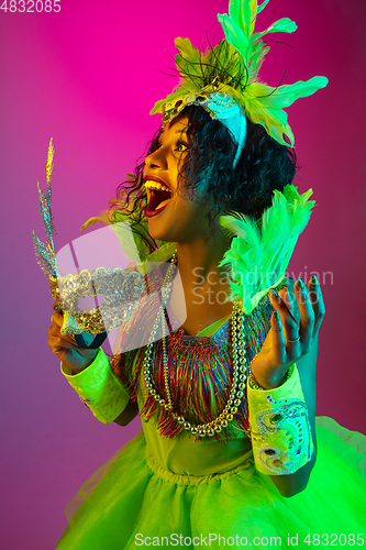 Image of Beautiful young woman in carnival and masquerade costume on gradient studio background in neon light