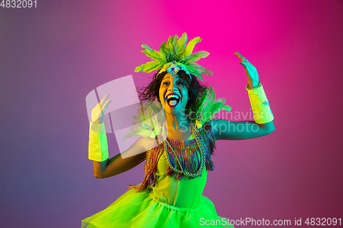 Image of Beautiful young woman in carnival and masquerade costume on gradient studio background in neon light