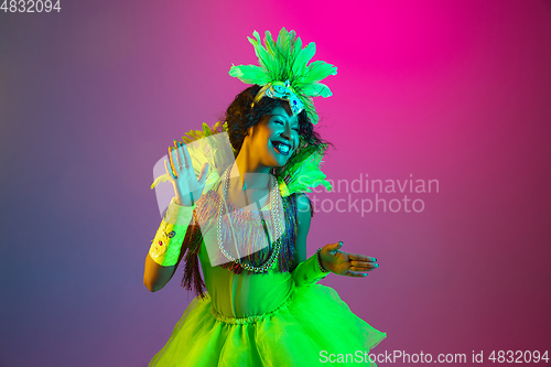 Image of Beautiful young woman in carnival and masquerade costume on gradient studio background in neon light