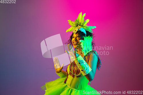 Image of Beautiful young woman in carnival and masquerade costume on gradient studio background in neon light