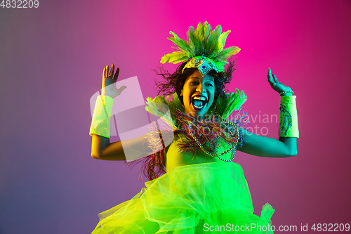 Image of Beautiful young woman in carnival and masquerade costume on gradient studio background in neon light