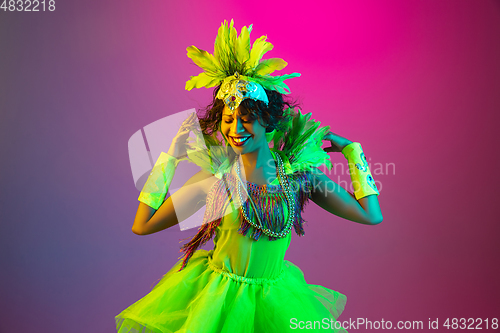 Image of Beautiful young woman in carnival and masquerade costume on gradient studio background in neon light