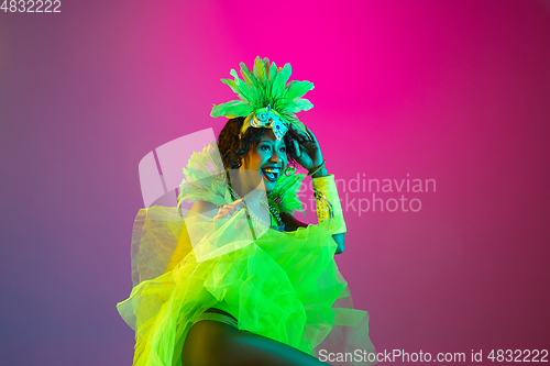 Image of Beautiful young woman in carnival and masquerade costume on gradient studio background in neon light