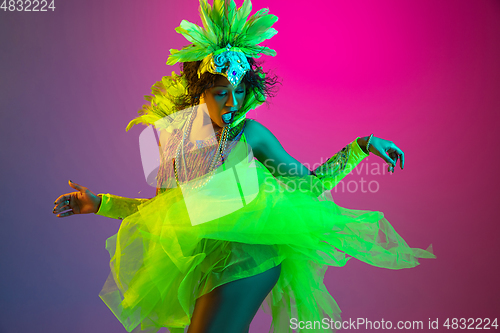 Image of Beautiful young woman in carnival and masquerade costume on gradient studio background in neon light