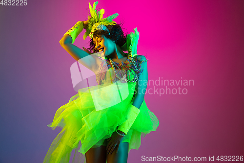 Image of Beautiful young woman in carnival and masquerade costume on gradient studio background in neon light