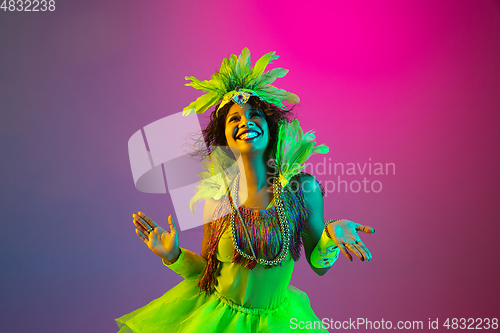 Image of Beautiful young woman in carnival and masquerade costume on gradient studio background in neon light