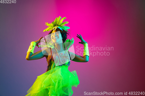 Image of Beautiful young woman in carnival and masquerade costume on gradient studio background in neon light