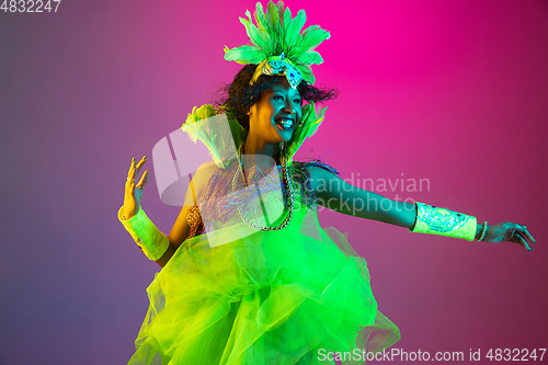 Image of Beautiful young woman in carnival and masquerade costume on gradient studio background in neon light