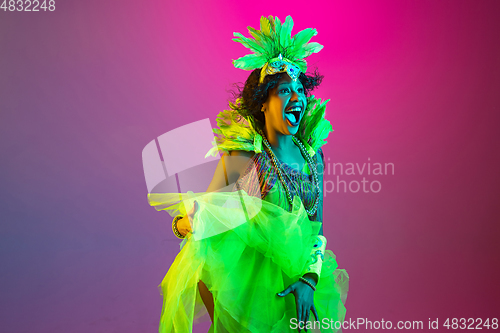 Image of Beautiful young woman in carnival and masquerade costume on gradient studio background in neon light