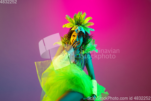 Image of Beautiful young woman in carnival and masquerade costume on gradient studio background in neon light