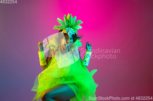 Image of Beautiful young woman in carnival and masquerade costume on gradient studio background in neon light